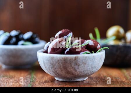 Verschiedene Oliven mit frischem Rosmarin auf rustikalem Holzhintergrund. Nahaufnahme. Stockfoto