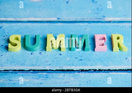 Das Wort Sommer legte mit farbigen hölzernen Buchstaben auf blauem Hintergrund mit Kopierraum Stockfoto