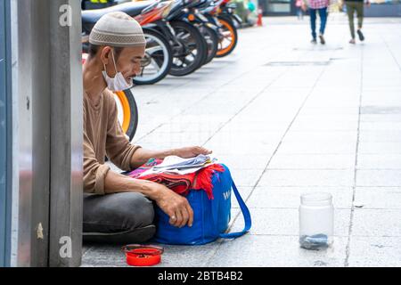Ein Mann bittet um eine Geldspende auf einer Stadtstraße. Ein Mann sitzt auf dem Bürgersteig neben einer SpendenDose. Stockfoto