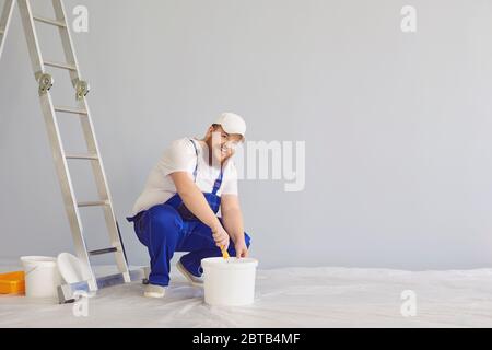 Malermalerei. Lustige dicke bärtige männliche Hausmaler mit einem Rollschuh stehend Farben im Hintergrund. Malerei Reparatur Dekorateur Wand zu Hause Stockfoto