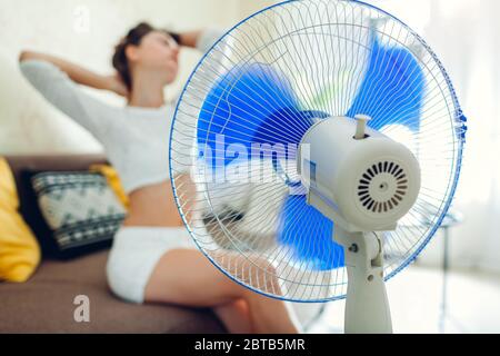 Sommerhitze. Klimaanlage. Junge Frau kühlt sich heiss fühlen sitzen auf der  Couch durch Ventilator zu Hause Stockfotografie - Alamy