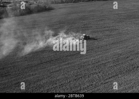 Ein Raupentraktor kultiviert den Boden in einem landwirtschaftlichen Feld. Draufsicht Fliegen auf einer Drohne. Diagonalwinkel in schwarz-weiß. Stockfoto