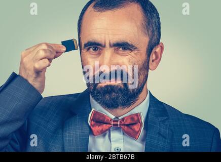 Konzept für externen Speicher erforderlich. Porträt des skeptischen bärtigen Geschäftsmann trägt elegante Jacke, rote Fliege hält Micro SD-Karte in der Nähe seines Kopfes isol Stockfoto