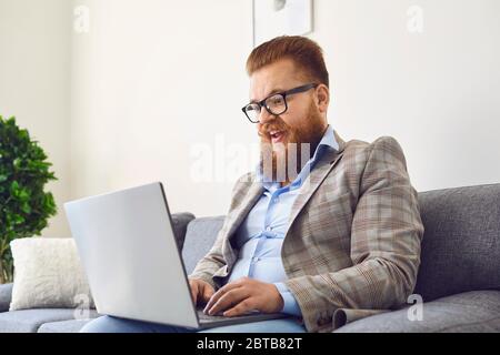 Online arbeiten. Lustige bärtige Mann in Brille lachen Arbeit Online-Video-Chat-Anruf mit Laptop im Home Office. Stockfoto