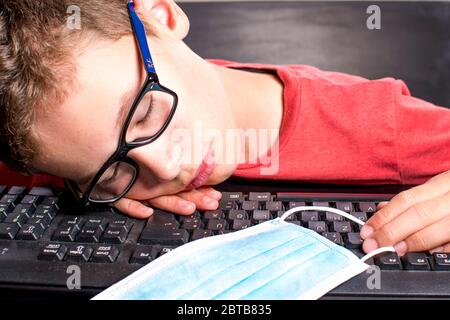 Kind schläft über Tastatur mit Mundschutz ein Stockfoto