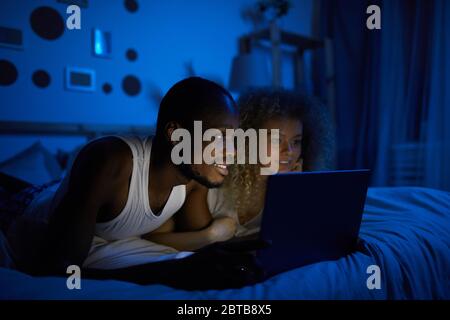 Porträt des jungen Mischrassenpaares mit Laptop während der Nacht im Bett liegen und Filme ansehen, kopieren Raum Stockfoto