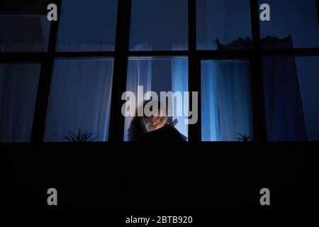 Weitwinkel Seitenansicht bei jungen lockigen Frau sitzt auf dem Fenster eine Nacht und mit Smartphone, kopieren Raum Stockfoto