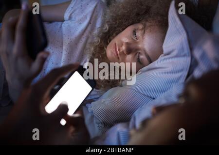 Porträt von lockig-haarigen jungen Frau mit Smartphone während mit Freund im Bett in der Nacht liegen, kopieren Raum Stockfoto