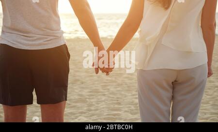 Glückliche junge Frauen und Männer Figuren verbinden Hände auf leeren Strand am windigen Tag im tropischen Resort Nahaufnahme Rückseite Blick Stockfoto
