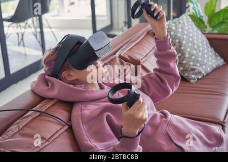 Hipster teen Mädchen tragen vr Headset halten Controller spielen virtuelle Realität auf dem Sofa. Stockfoto
