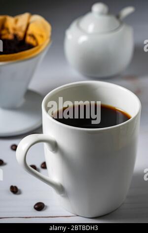 Kaffeebecher mit schwarzem Kaffee und einem Übergiessfilter im Hintergrund. Stockfoto