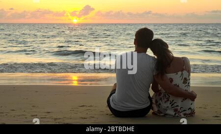 Ein schönes junges Paar umarmte sich am leeren Strand am Meer und beobachtete den Sonnenuntergang im tropischen Resort am Abend mit Blick auf den Rückseitenbereich Stockfoto