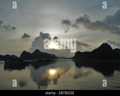 Sonnenuntergang, Berge und eine Bootsspiegelung auf dem Wasser in Ha Long Bay in Vietnam Stockfoto