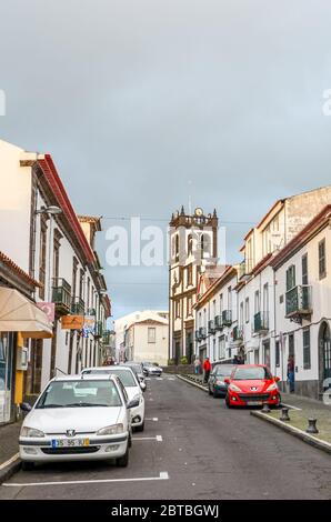 Lagoa, Azoren, Portugal - 13. Jan 2020: Stadtstraße im Fischerdorf Lagoa. Geparkte Autos auf der Asphaltstraße, traditionelle Gebäude und Kirche im Hintergrund. Vertikales Foto. Stockfoto