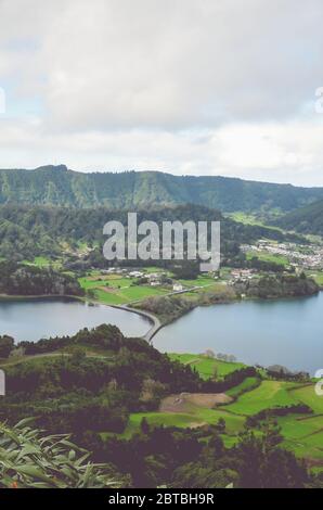 Herrlicher Blick auf die Lagoa Azul und das Dorf Sete Cidades vom Aussichtspunkt Miradouro do Cerrado das Freiras in Azoren, Portugal. Seen umgeben von grünen Feldern und Wald. Vertikales Foto. Stockfoto