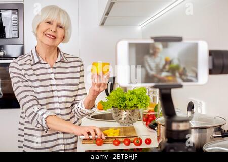 Ältere Frau hält Pfeffer, Aufnahme Online-Video mit Kochkurs Stockfoto