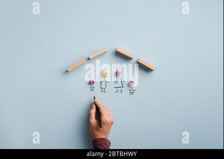 Familienversicherung und Sicherheit konzeptionelles Bild - männliche Hand Zeichnung einer Familie unter einem Dach aus Holzblöcken. Stockfoto