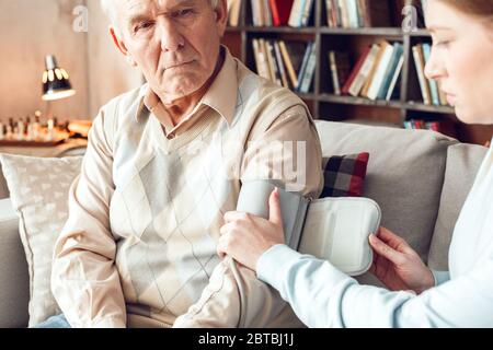 Vater und Tochter zu Hause Bibliothek sitzende Frau wickeln die Manschette um den Arm Stockfoto