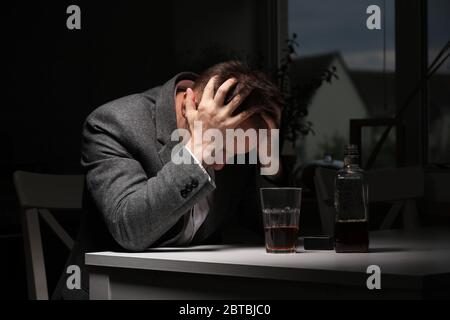 Mann, der Alkohol in der Küche trinkt. Junger Mann mit starken Kopfschmerzen oder Migräne sitzt mit einem Glas Whisky in der Küche. Alkohol hängt ab Stockfoto