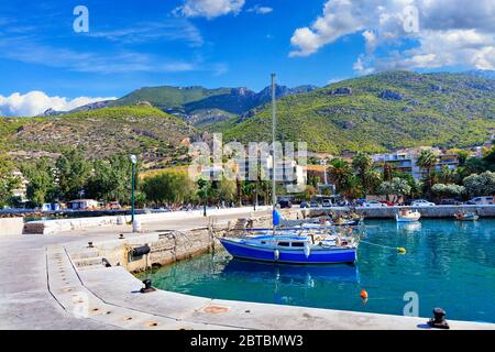 Landschaftlich schöne Aussicht auf die Bucht und den Pier Loutraki, Griechenland, wo kleine Fischerboote, Yachten, Boote und Boote im klaren Wasser des Ionischen Meeres festgemacht sind. Stockfoto