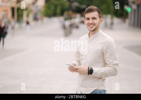Schöner junger Mann, der sein Telefon im Zentrum der Stadt benutzt. Mann, der Online-Spiele im Freien spielt Stockfoto
