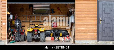 Fassade Vorderansicht Tür öffnen ATV Quad Bike Motorrad Parkplatz chaotisch Garage Gebäude mit Holzverkabelung zu Hause Auffahrt Hinterhof und Rasenweg. Haus Stockfoto