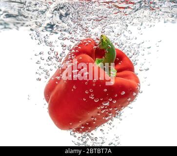 Saftig rot ökologische, Pfeffer fällt in sauberes Wasser erzeugt Blasen. Isoliert auf weißem Hintergrund. Stockfoto