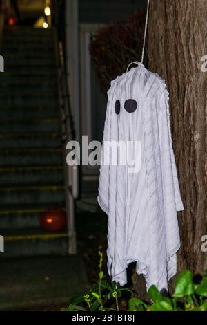 Weißer Geist hängt an einem Baum während eines Urlaubs für Halloween auf dunklem Hintergrund. Stockfoto