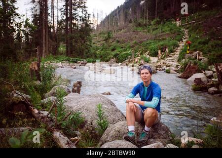 Mädchen Tourist Sedin auf dem Stein in der Nähe des Berges Fluss in der Hohen Tatra in der Slowakei. In einem blauen T-Shirt, grauen Shorts, Wanderschuhe gekleidet Stockfoto