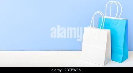 Weiße blaue Handarbeitspapiertaschen. Shopping Mockup Taschen Papier-Pakete auf weißem Tisch blaues Licht Hintergrund mit Kopierraum. Einkaufen, Verkauf, Lieferung von Lebensmitteln Stockfoto