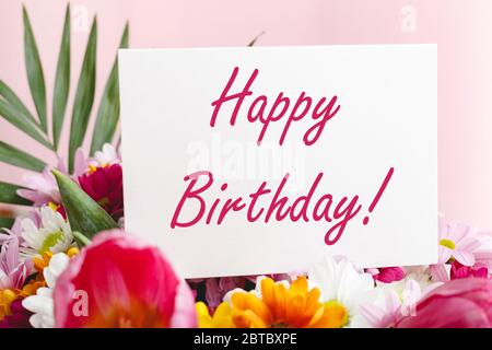 Happy Birthday Text auf Karte in Blumenstrauß auf rosa Hintergrund. Blumenversand, Glückwunschkarte. Grußkarte in Tulpen, Gänseblümchen Stockfoto