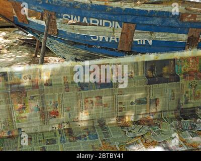 Moderne Glasfaser-Bootsbau mit Zeitungspapier kontrastiert mit Umbau der traditionellen hölzernen geschälten Schiff an Strand Bootswerft Malindi, Kenia, Afrika Stockfoto