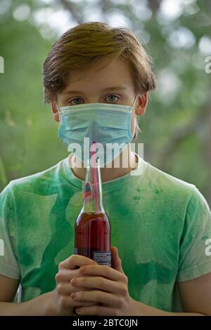 Junge mit Atemmaske trinken aus einer Flasche mit einem Stroh, Deutschland Stockfoto