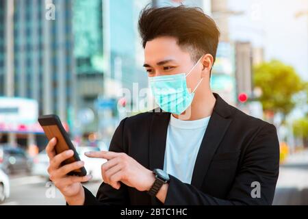 Junger Geschäftsmann, der auf der Straße eine Maske trägt und das Handy zwickern kann Stockfoto