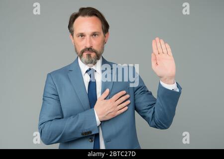 Ich schwöre. Senior Anwalt machen Eid grauen Hintergrund. Reifer Mann hält Hand am Herzen und offene Handfläche. Versprechen der Treue. Wirtschaftsanwalt. Rechtsanwalt oder Rechtsanwalt. Recht und Gerechtigkeit. Guter Anwalt kennt Recht. Stockfoto