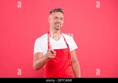 Glücklicher Unternehmer des Kaffeehaus. Der Barista ist männlich und trägt Uniform. Der unrasierte Mann arbeitet als Barista. Teilzeitjob. Selbstbewusster Barista Mann zeigt Finger. Reife erfahrene Barista tragen rote Schürze. Stockfoto