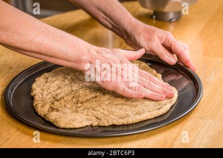 Sobald der Pizzateig so weit wie möglich in der Luft gestreckt wurde, glätten Sie ihn mit den Händen, beginnen Sie in der Mitte und arbeiten Sie nach außen, verwenden Sie y Stockfoto