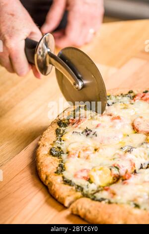 Frau mit einem Pizzaschneider, um eine frisch gebackene, vegetarische, Pesto, Multi-Grain, dick-Kruste Pizza schneiden Stockfoto