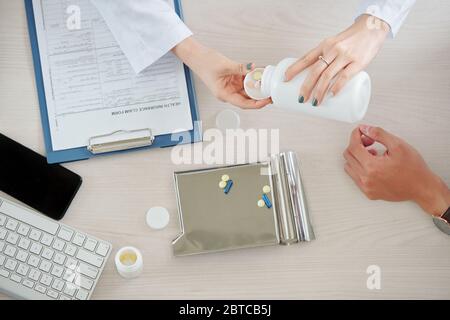 Arzt gibt Patienten einige Schmerzmittel, Ergänzungen und Vitamine nach Überprüfung seiner Versicherung, Ansicht von oben Stockfoto