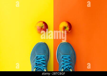 Blaue Sneaker und Äpfel auf gelborangenem Hintergrund. Konzept für einen gesunden Lebensstil, tägliches Training und gute Ernährung. Flaches Lay, Kopierbereich. Stockfoto