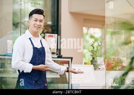 Porträt des jungen positiven vietnamesischen Mann begrüßt Kunden in seinem Café Stockfoto