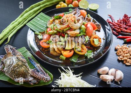 Würziger Seafood-Salat mit Krabbenmuscheln auf schwarzem Teller mit frischem Gemüse, Kräutern und Gewürzen / Menü Thai Food Stockfoto