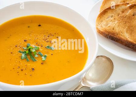Kürbissuppe in weißer Schüssel mit geröstetem Brot an der Seite Stockfoto