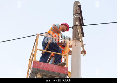 Elektriker an den Säulen montieren die Halterung für die Stromleitung. Professionelle Elektriker arbeiten am Turm. Stockfoto