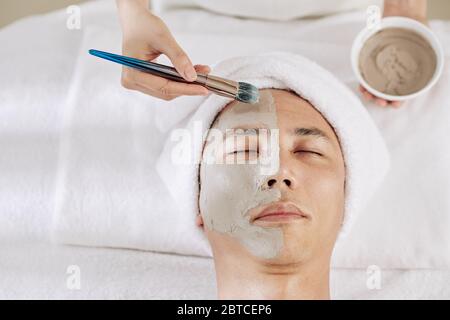 Kosmetologe Anwendung Ton Maske auf die Hälfte des Gesichts der männlichen Client Stockfoto