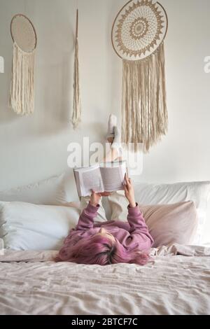 Teen Mädchen mit rosa Haar im Bett liegend halten Füße hoch Buch lesen. Stockfoto