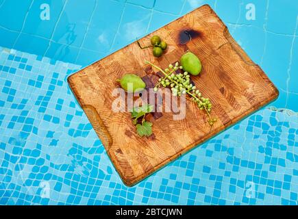 Frische grüne unreife Trauben, Mandarinen und Mangos auf einem Holzhintergrund in blauem Wasser und Kopierraum. Stockfoto