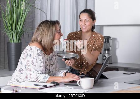 Lachende junge Frau, die eine Gabel mit einem Bissen Essen hält, während eine andere Frau nach vorne greift, um sie zu greifen. Home Office und Kochkonzept. Stockfoto