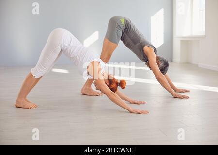 Mann und Frau mittleren Alters stehen in Hundestellung während Gemeinsam Yoga im hellen Fitnessraum üben Stockfoto