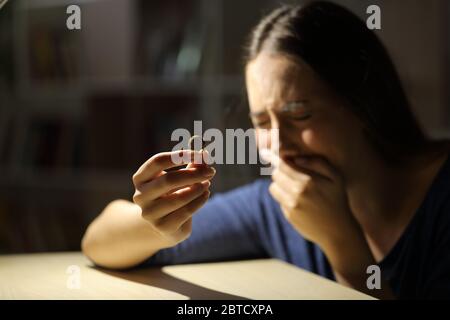 Traurige Frau weinend einen Ehering haltend beschwerend allein in der Nacht zu Hause sitzen Stockfoto